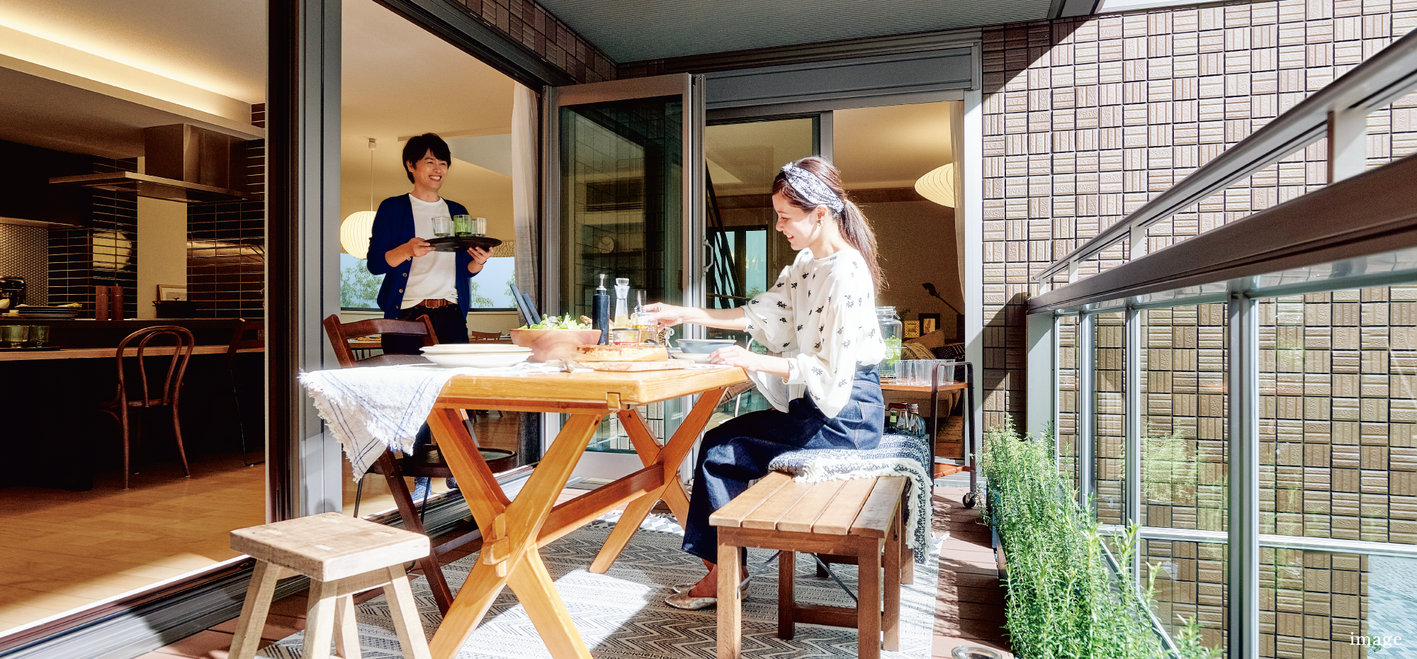 バルコニーで食事をする女性と、料理を運んでくる男性の写真