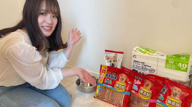 床に並べた犬用おやつやペットシーツを指し示す女性の写真