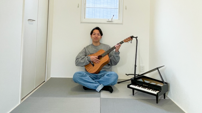 ギターを弾く男性と、隣に置かれた小型ピアノの写真